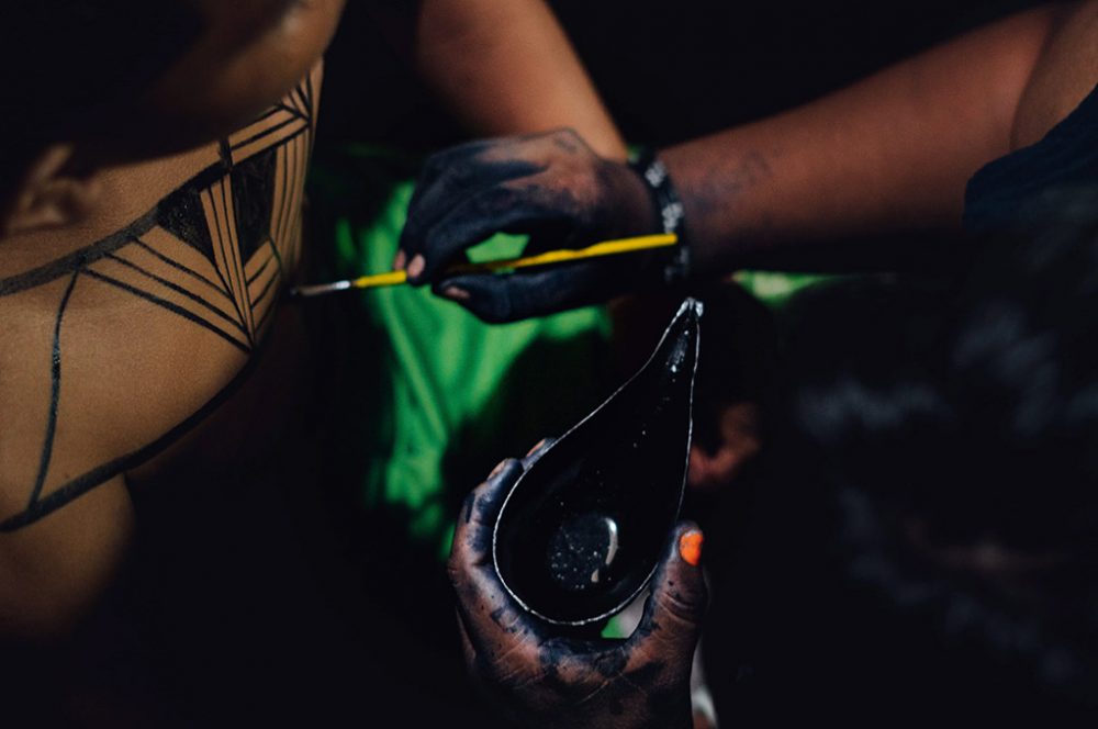 Traços indígenas sendo pintados no corpo de um jovem.